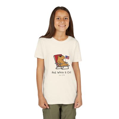 A young girl wearing a Capy Life cream-colored youth t-shirt featuring a capybara lounging with an American flag.