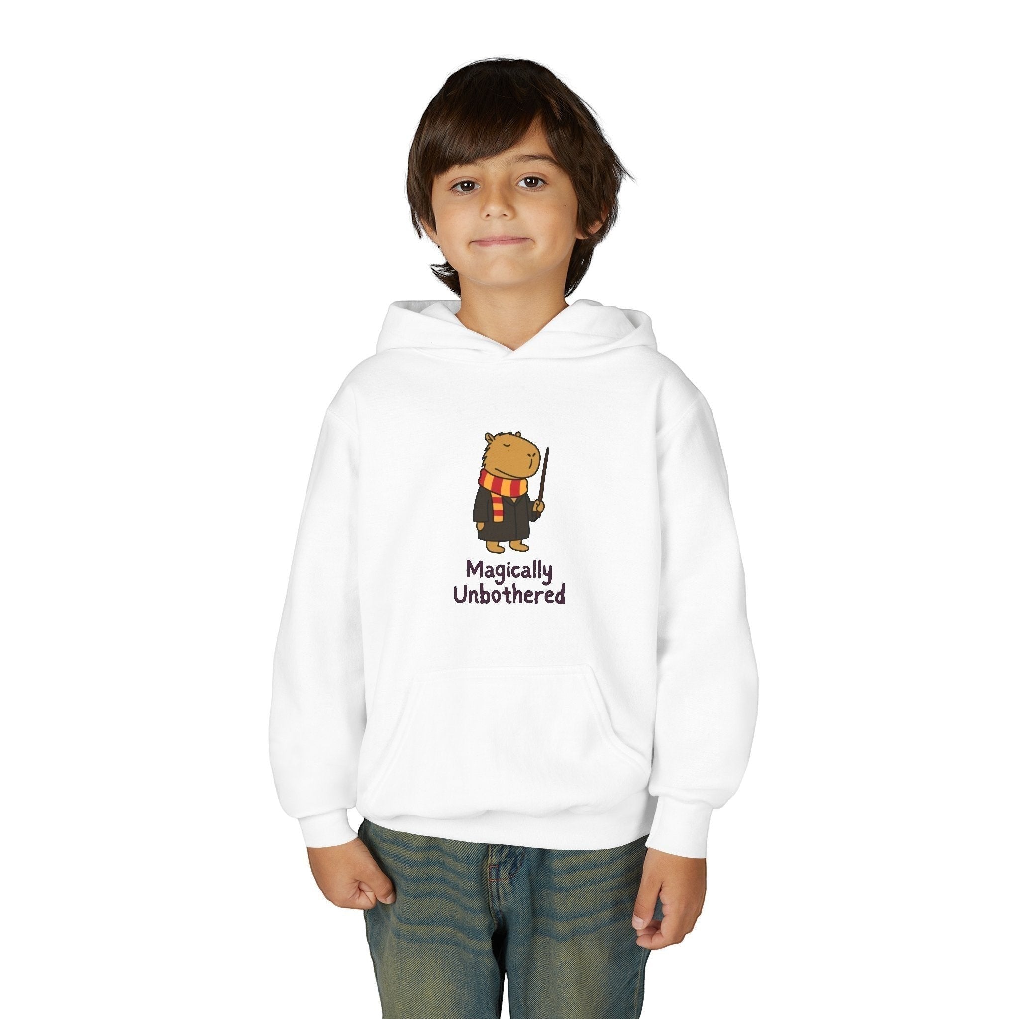 A child wearing a white Capy Life hoodie featuring a cute capybara wizard graphic with the text Magically Unbothered.