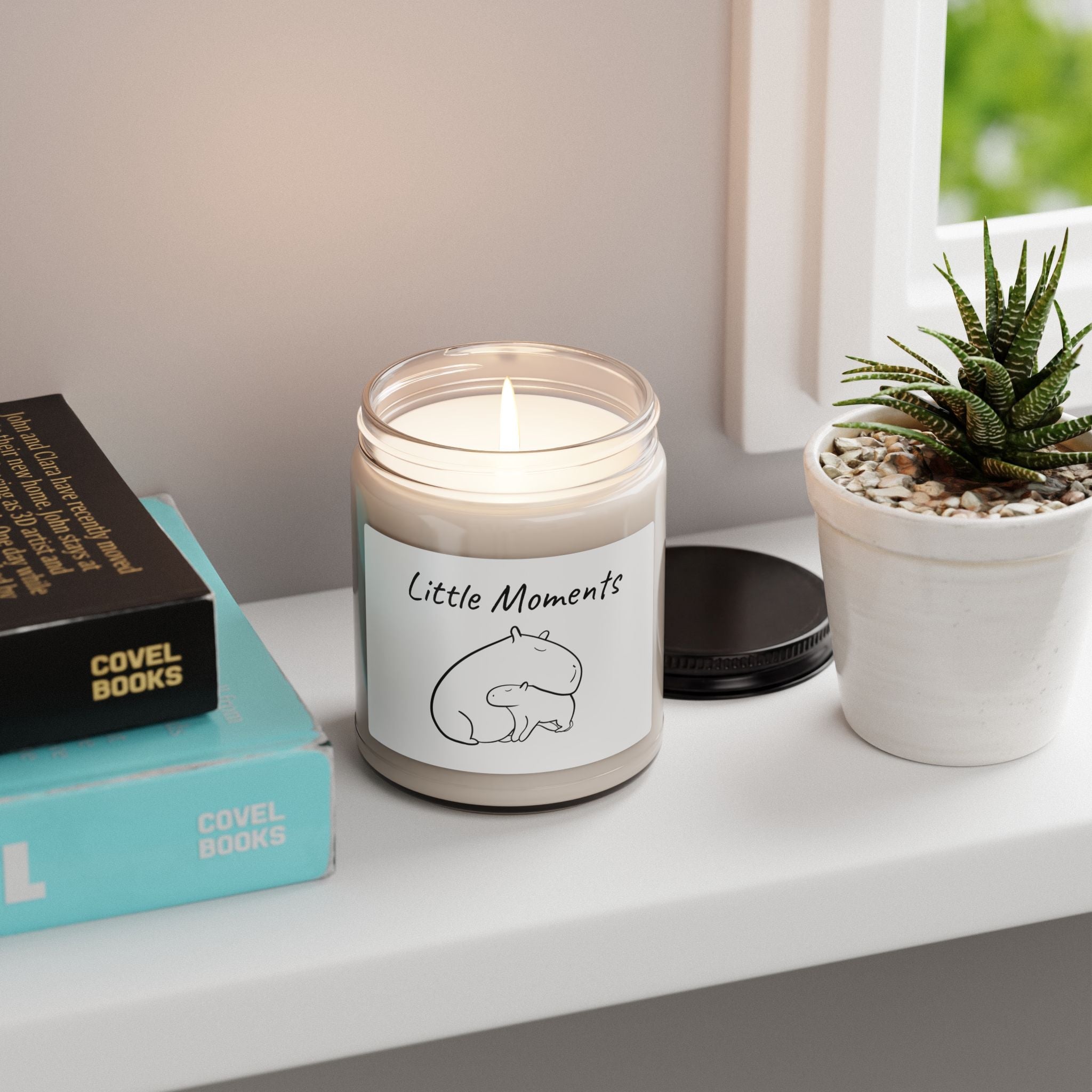 Capy Life soy wax candle in a glass jar with a minimalist capybara illustration, sitting on a windowsill.