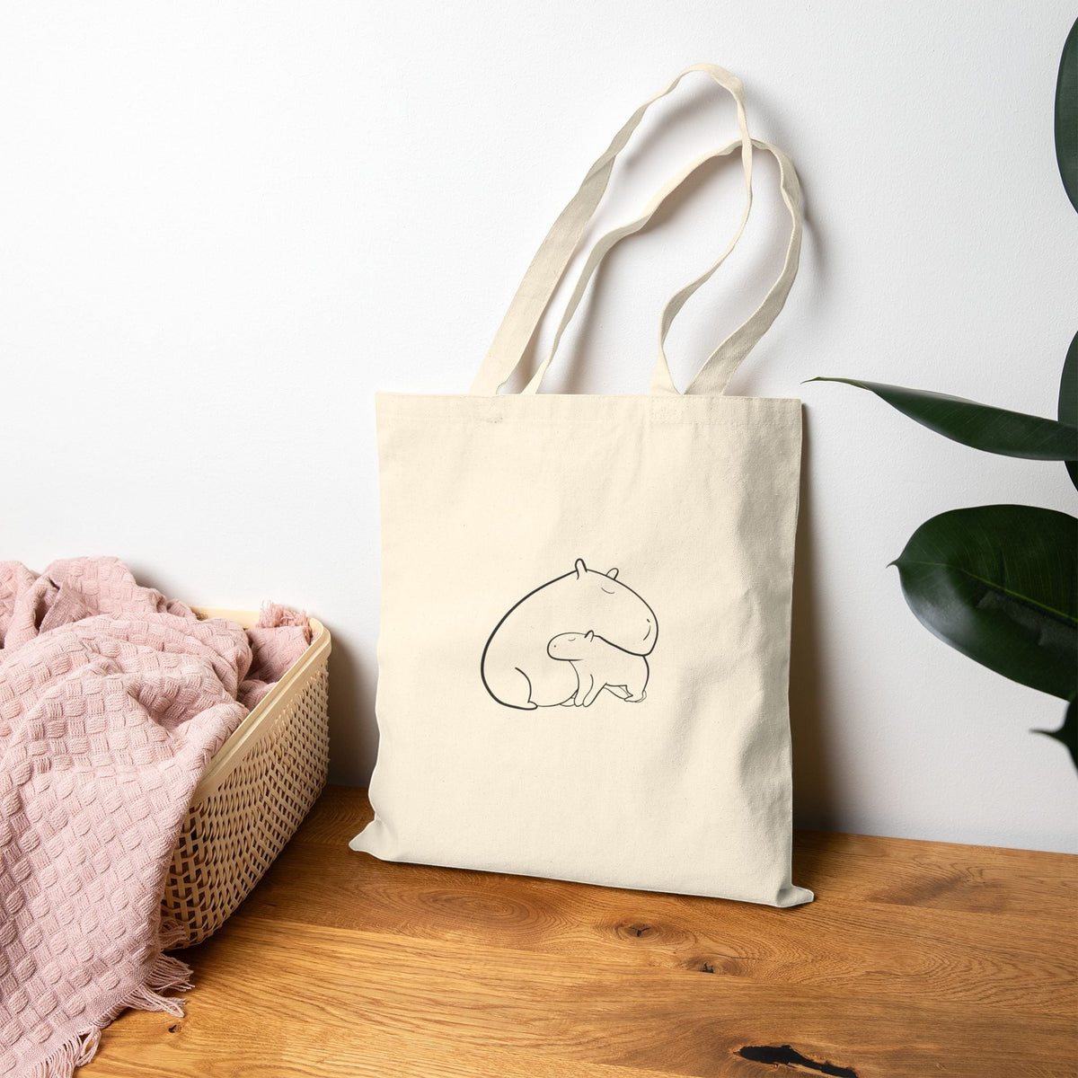 Capy Life natural cotton canvas tote bag featuring a minimalist line drawing of a mother and baby capybara snuggling.