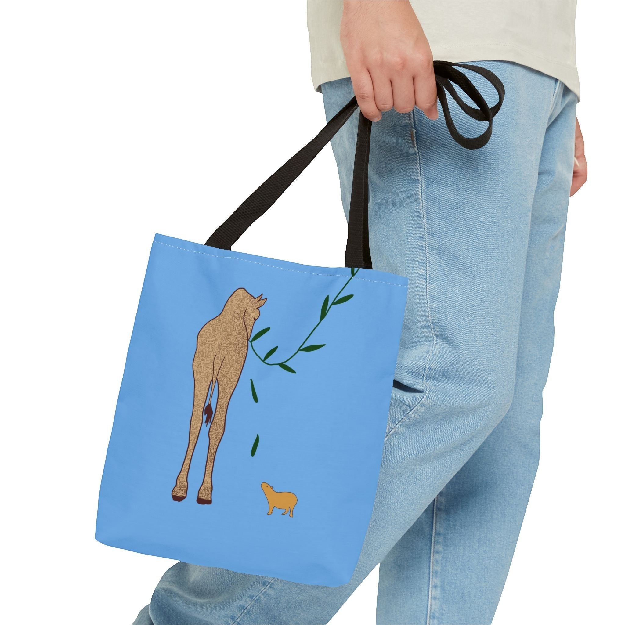 Capy Life minimalist tote bag in light blue with a capybara and giraffe illustration, held by a person in jeans.