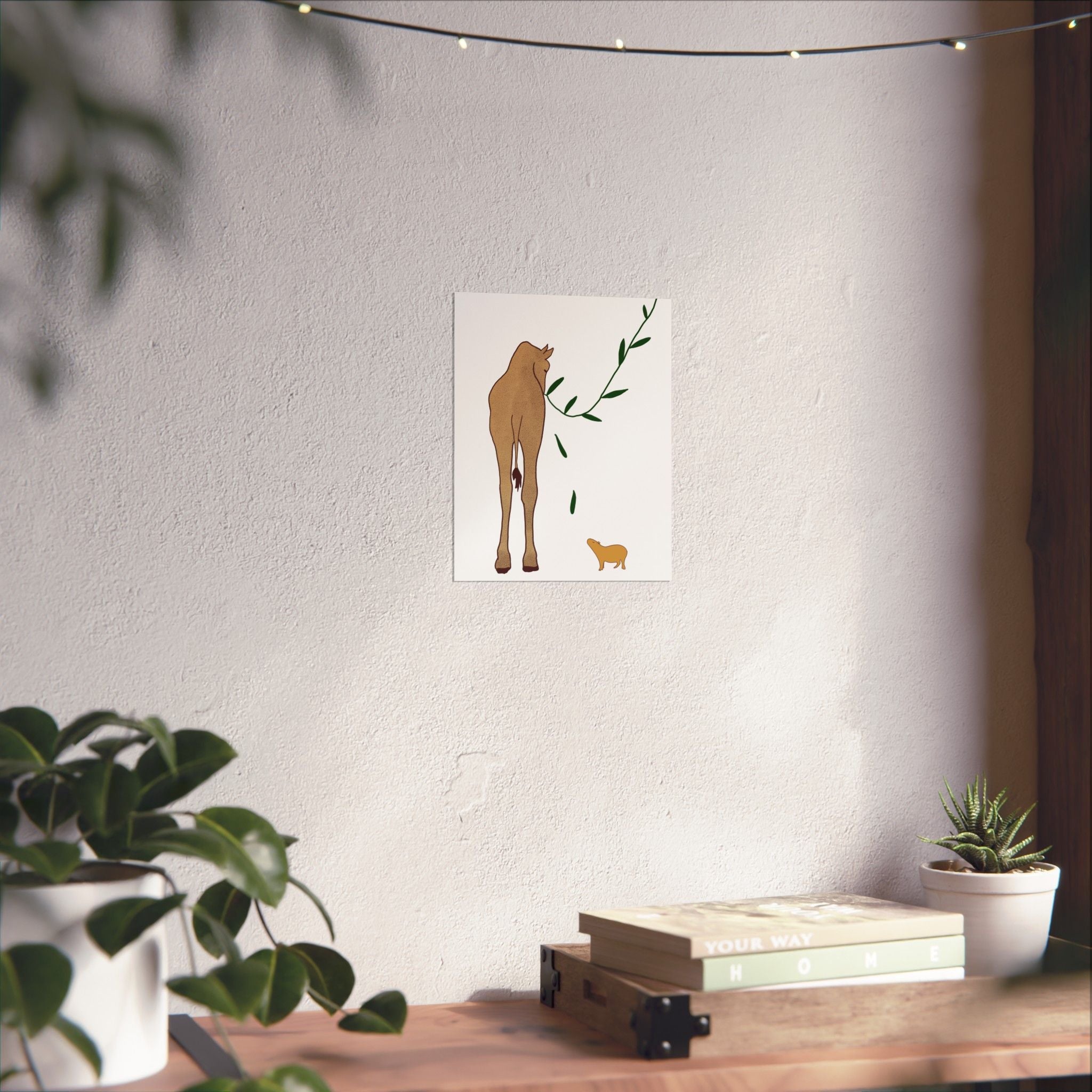 Capy Life minimalist wall art print featuring a giraffe and capybara on a neutral wall above a wooden shelf with plants