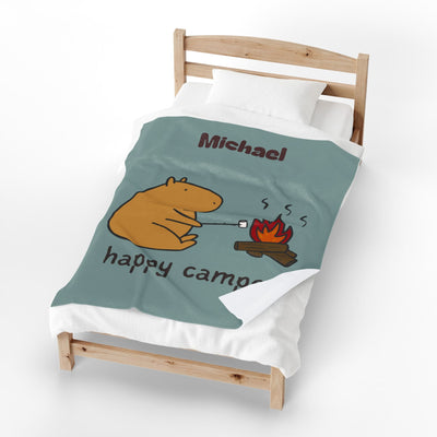 Capy Life personalized sage-green blanket featuring Gene the Capybara roasting a marshmallow by a campfire on a bed.