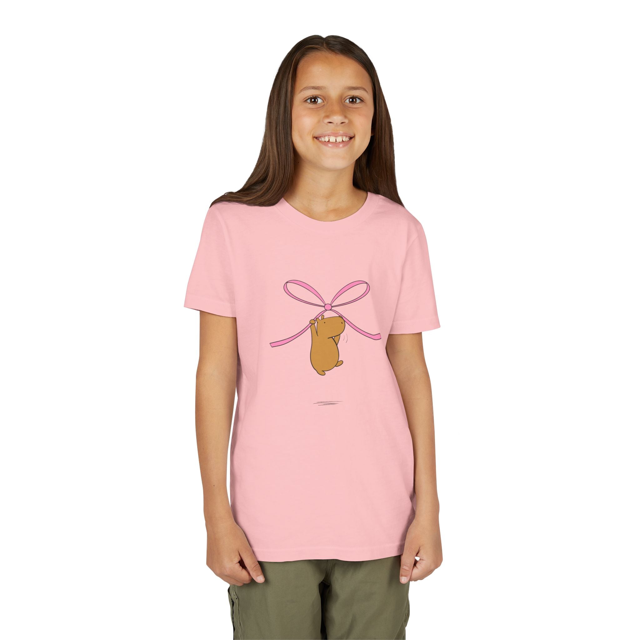 Capy Life kids pink t-shirt featuring a cute capybara hanging from a pink coquette bow graphic on a smiling girl