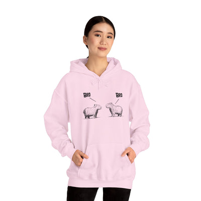 A woman wearing a light pink Capy Life pullover hoodie featuring a sketch of two capybaras with the text Bro above each.