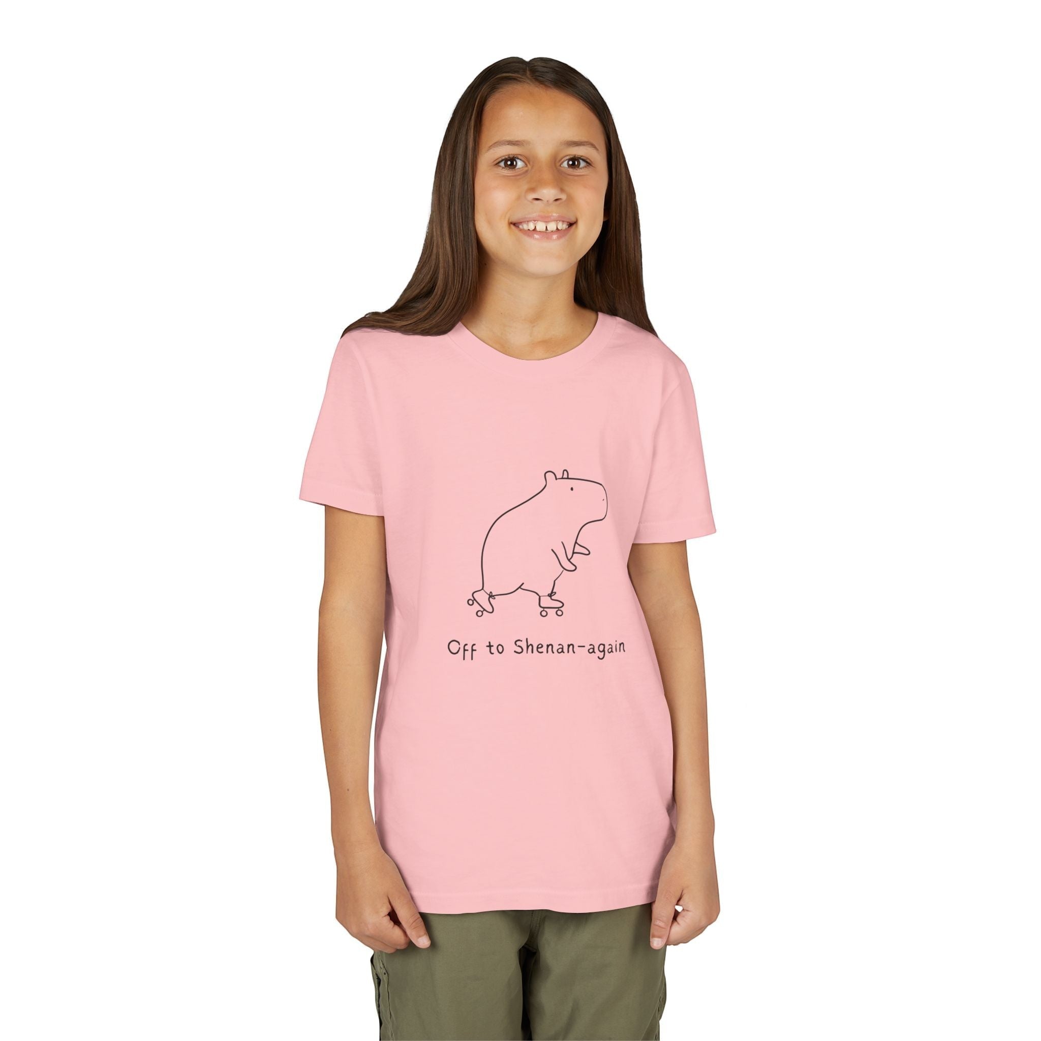 A smiling girl wearing a light pink Capy Life kids graphic tee featuring a cute capybara on roller skates.