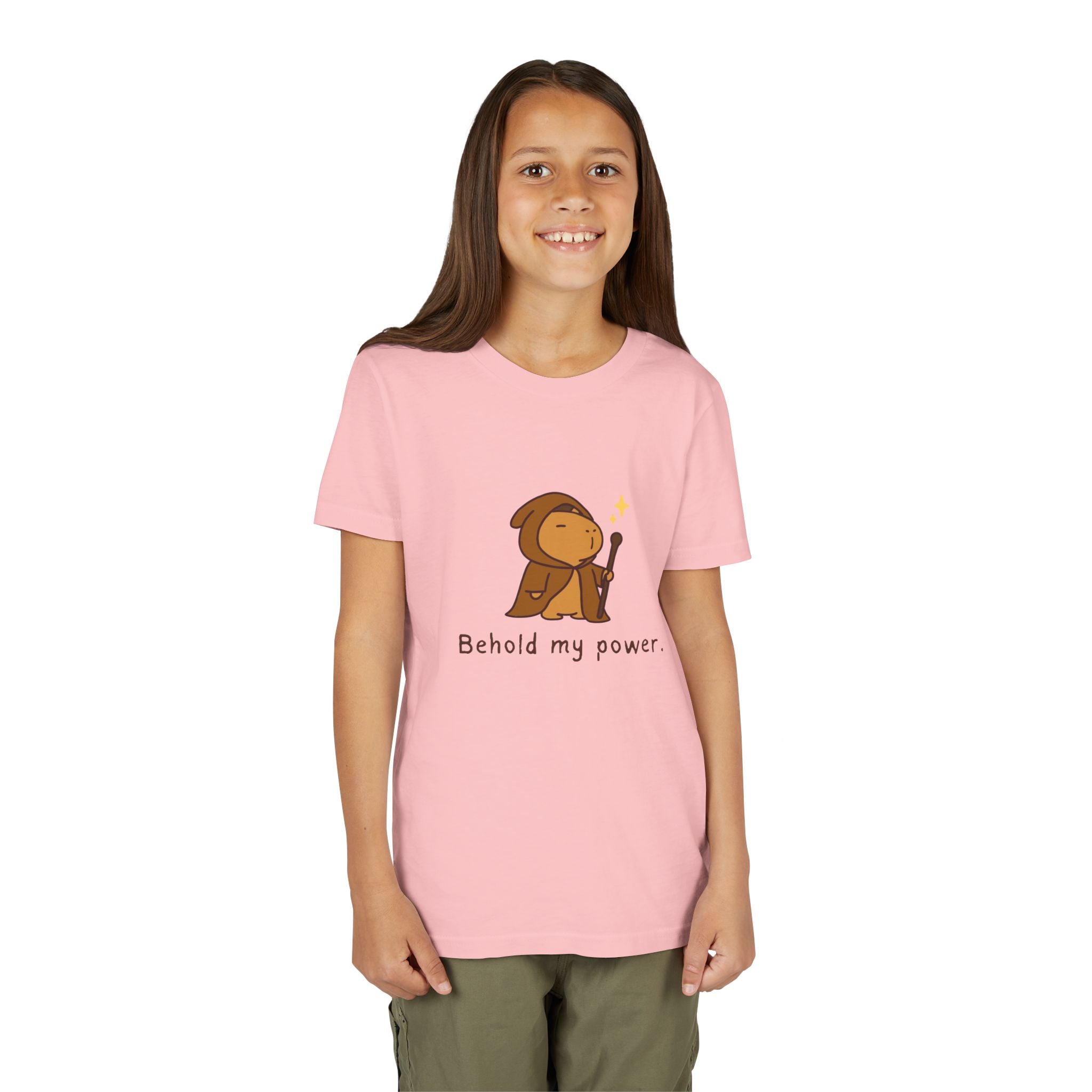 A young girl wearing a Capy Life light pink cotton t-shirt featuring a cute wizard capybara graphic and Behold my power text.
