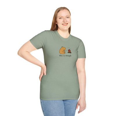 A woman wearing a sage green Capy Life softstyle t-shirt featuring a capybara roasting a marshmallow by a campfire.