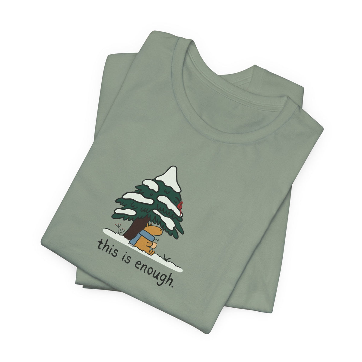 Capy Life sage green graphic t-shirt featuring a capybara in a blue scarf under a snowy evergreen tree.