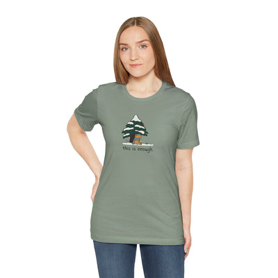Woman wearing a Capy Life sage green t-shirt with a graphic of a capybara under a snowy tree and the text this is enough