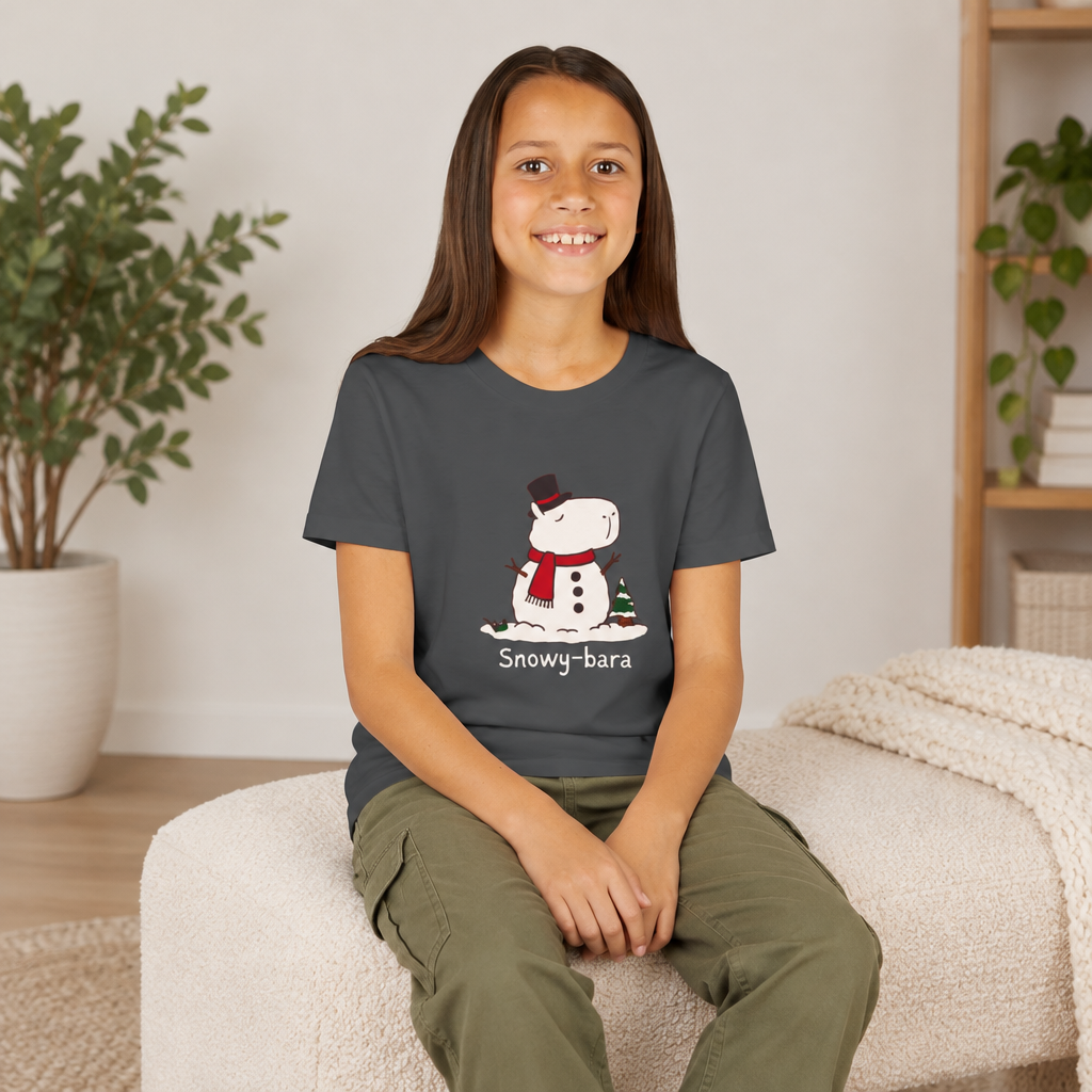 A young girl wearing a dark grey Capy Life youth t-shirt featuring a cute Snowy-bara snowman capybara illustration.
