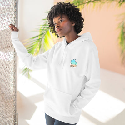 Capy Life white hoodie with a small, minimalist coastal capybara graphic worn by a woman near a fence.