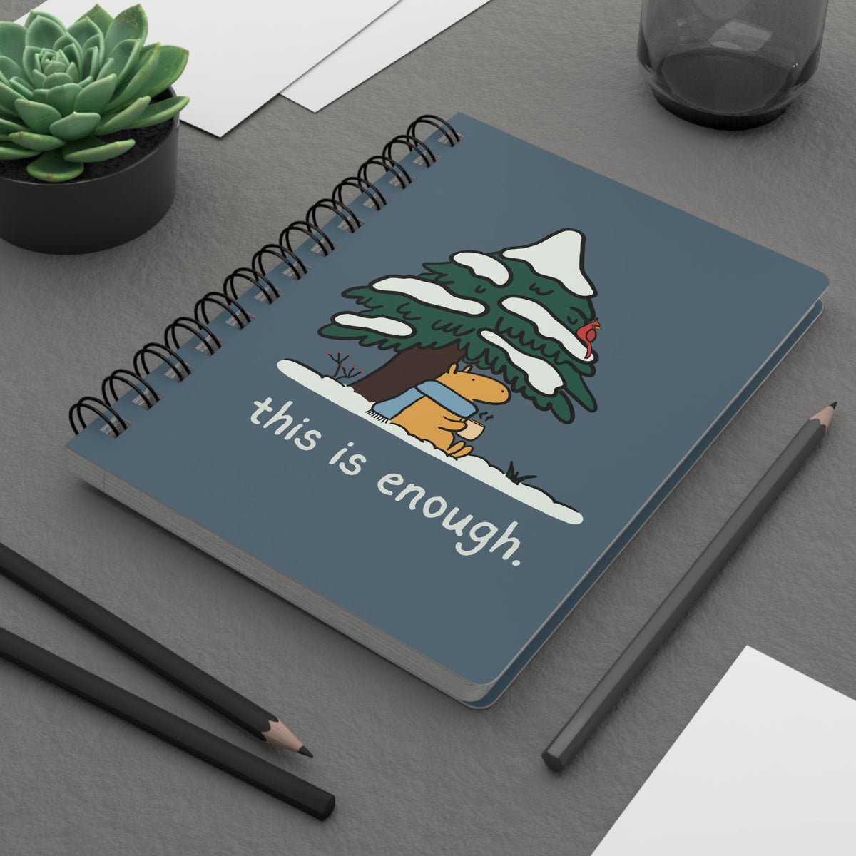 Capy Life spiral notebook with a blue cover featuring a capybara in a scarf under a snowy tree and winter text.